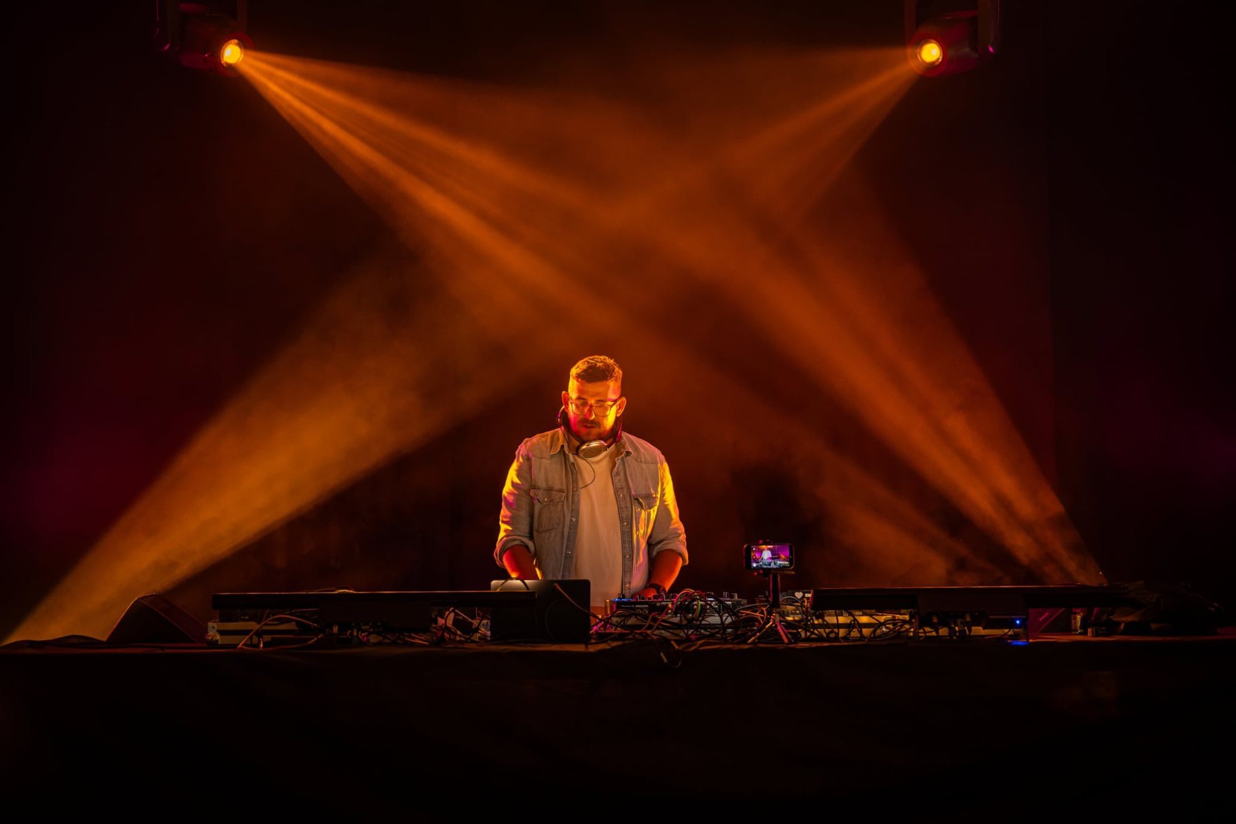 DJ JUVI na pódiu, zkřížené oranžové reflektory